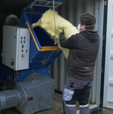 man with mask filling insulation into insulation compactor