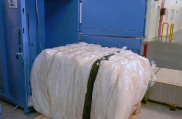 Plastic bale secured with black banding, freshly ejected from a blue baler at Trivium Packaging
