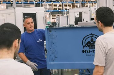 ABB Frosinone employee standing by a baler door, demonstrating its operation to two dark-haired men
