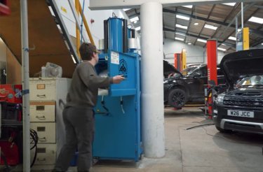 man putting cardboard in a baler in automotive repair shop