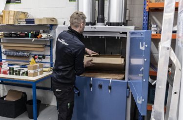 man puts cardboard in vertical baler