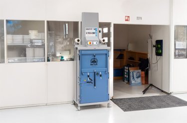 e119 blue electric baler standing against wall with windows